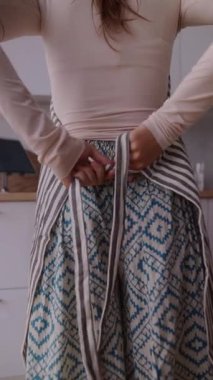 Modern bir mutfakta bir kadın önlüğünü ustalıkla düzeltir, güzel ve karmaşık desenlerle süslenir.