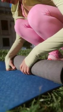 Genç bir kadın yoga minderini çimlerin üzerine seriyor, doğanın güzelliğinin ortasında dinlendirici bir uygulamaya hazır.