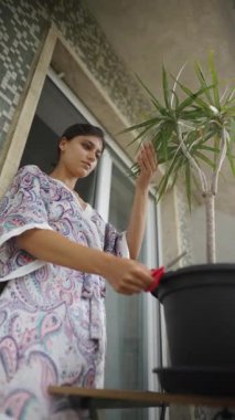 Bir kadın güzel ve zarif bir bornoz giyerken titizlikle balkonundaki saksıyı buduyor.