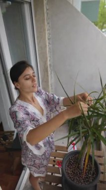 Bir kadın, balkondaki canlı bitkisini sevgiyle önemser. Bahçe işlerine olan tutkusunu gösterir.
