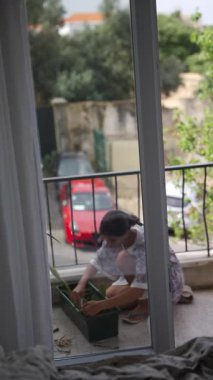 Küçük bir çocuk güneşli bir balkonda bahçıvanlık yapmaktan, bitkileri yetiştirmekten, yaratıcılığını ve doğasını göstermekten hoşlanır..