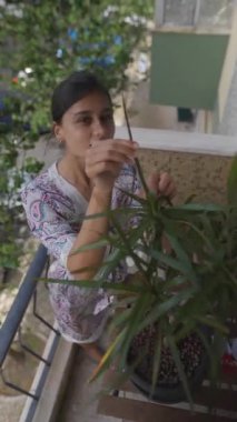 Balkonda bir bitkiyle ilgilenen, doğal ışıkta kentsel bahçe ve bitki bakımını ön plana çıkaran bir kişi.