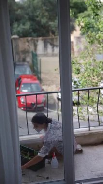 Bir insan, canlı bir dış görünüşü olan balkondaki çeşitli bitkilerle dikkatle ilgilenir.