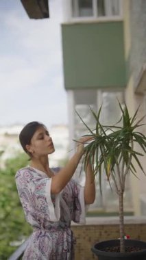 Bir kadın, rahat balkonunda canlı bir saksı bitkisini nazikçe besliyor. Huzurlu bir ev bahçesi sahnesi sergiliyor.