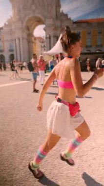 A happy young girl runs in colorful attire at a lively outdoor festival, showcasing a joyful spirit.