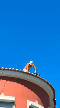 Çok yetenekli bir işçi, yukarıdaki parlak ve açık mavi gökyüzünün altında titizlikle çatıyı onarıyor.
