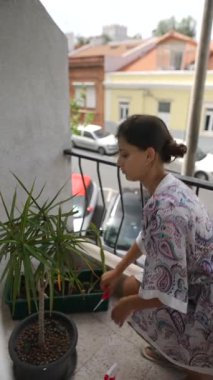 Güneşli bir günde, bir kadın büyüleyici bir balkonda canlı saksı bitkileriyle ilgilenir, açık havanın tadını çıkarır.