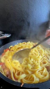 Bir tencere buharlı makarna, canlı, taze sebzeler ve sıcak tavada kremalı sosla karıştırılıyor.