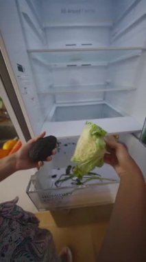 Neredeyse boş bir buzdolabında sebze organize eden bir insan sağlıklı yaşam tarzını ve beslenme seçeneklerini ön plana çıkarıyor.
