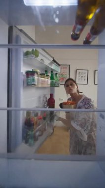 Bir kadın, sağlıklı yiyecek seçeneklerini düşünerek, buzdolabını iyice araştırmak için acele etmez.