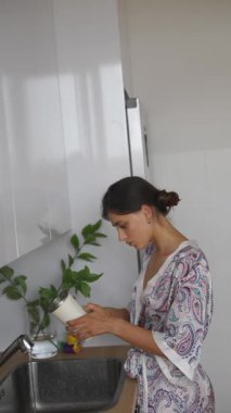 Renkli desenli bir bornoz giyen bir kadın şık ve şık bir mutfakta ustaca yemek hazırlıyor.