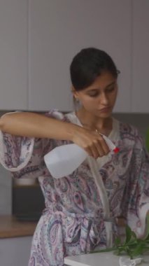 Kapalı alandaki bitkilerini nazikçe buğulandıran bir kadın, modern evindeki yeşillik ve bakımı çok güzel bir şekilde sergiliyor.