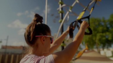 Bir kadın güneşli bir gökyüzünün altında süspansiyon kayışları kullanarak canlandırıcı bir açık hava egzersizinden mutlu bir şekilde zevk alıyor.