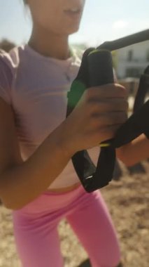 Direniş bantlarını kullanarak canlı ve çekici bir egzersiz rutini açık havada dinamik pembe kıyafetlerle sergileniyor.