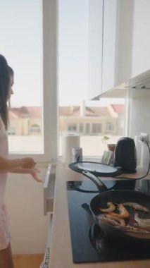 Bir kadın güzel doğal ışıkla dolu şık mutfağında ustalıkla deniz ürünleri pişirir.