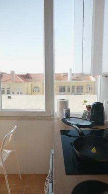 Neşeli bir mutfak sahnesi. Pencerenin kenarında kahvaltı hazırlayan bir kadın. Güneşli sabah ışığının tadını çıkarıyor.