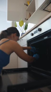 Mavi eldiven giyen bir kadın güzel, parlak ve şık bir mutfakta fırınını titizlikle temizliyor.