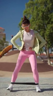 Bir kadın canlı bir açık hava ortamında renkli direnç bantları kullanarak aktif olarak çeşitli egzersizler yapıyor.