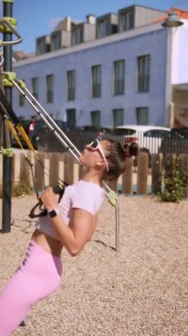 Kararlı bir kadın, gücünü ve zindeliğini arttırmak için açık havada güneş ışığında süspansiyon egzersizleri yapıyor.