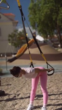 Bir kadın güzel, enerjik bir açık hava ortamında güç ve esneklik sağlamak için TRX egzersizi yapıyor.