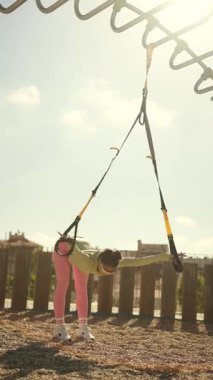 Açık hava ortamında TRX kayışları kullanan dinamik bir fitness oturumu, güç ve esneklik göstergesi.