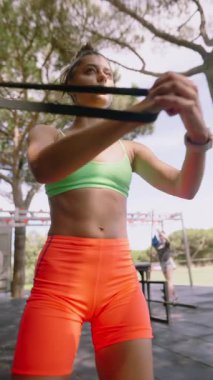 Formda bir insan dışarıda renkli direniş bantlarıyla egzersiz yapıyor ve canlı bir spor kıyafeti giyiyor.