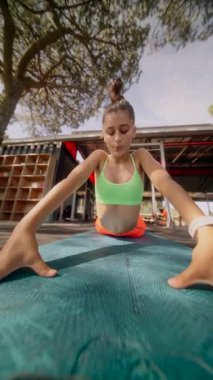 Yoga yapan genç bir kadın dışarıda minderinin üzerinde geriliyor, sağlığı, sükuneti ve sağlığını destekliyor.