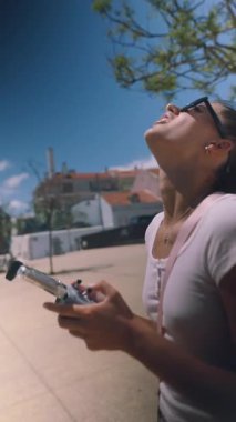 Genç bir kadın güneşli bir günün tadını çıkartıyor. İnsansız hava aracını ustalıkla kontrol ediyor. Açık hava teknolojisini canlı bir ortamda sergiliyor.