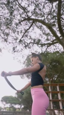 Bir kadın aktif olarak direniş bantlarını kullanarak egzersiz yapıyor. Etrafı çarpıcı, manzaralı bir ortam ile çevriliyken.