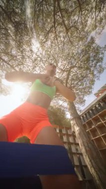 Çevresi ağaçlar ve güneş ışığıyla çevrili, dışarıda direniş bantlarıyla egzersiz yapan formda bir birey..