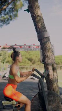 Genç bir kadın hareketsiz bir bisiklette spor kıyafetlerini sergileyerek dışarıda spor yapıyor..