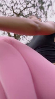 Bir kadın yoğun bir şekilde kürek çekme makinesinde çalışıyor, sakin bir açık hava ortamında egzersiz rutinine dalmış.