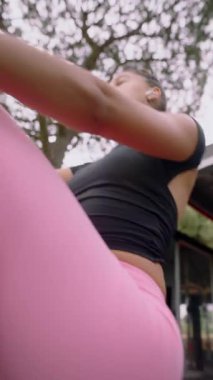 Genç bir kadın, canlı pembe taytlarıyla kürek çekme makinesinde egzersiz yapıyor, spor yaparken kendini gösteriyor..