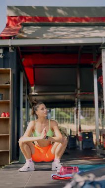 Genç bir kadın dışarıda çömeliyor, enerjik bir egzersiz rutininde zindelik ve kararlılık gösteriyor..