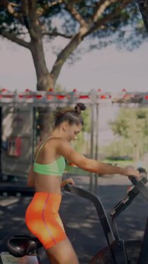 Genç bir kadın, aydınlık ve güneşli bir ortamda eliptik bir makinede hareketli ve canlandırıcı bir egzersizin tadını çıkarıyor.