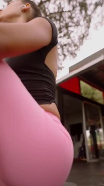 Bir fitness meraklısı açık havada canlı pembe tozluklarla kürek çekiyor ve siyah bir bluz giyiyor, sağlık ve enerjiyi somutlaştırıyor.