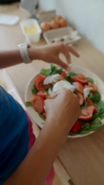 Taze ıspanaklı, sulu domatesli ve lezzetli malzemeli canlı bir salata yapan bir insan.