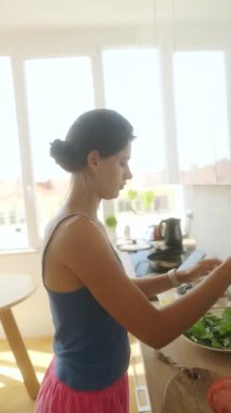 Güneşli güzel bir mutfakta, bir kadın taze ve canlı bir salata hazırlar, sağlıklı yemekleri ön plana çıkarır.