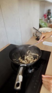 Bir insan, güzel bir mutfakta, modern bir indüksiyon sobasında taze mantarları ustalıkla pişiriyor.