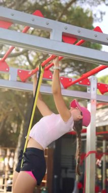 Genç bir kız renkli oyun parkı ekipmanlarına barfiks çekiyor. Gücünü ve çevikliğini gösteriyor.