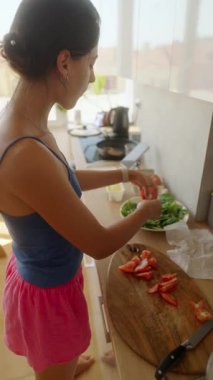 Bir kadın parlak bir mutfakta taze, renkli bir salata hazırlıyor. Sağlıklı aşçılık uygulamaları sergiliyor.