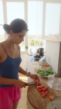 Bir kadın, modern mutfak alanında renkli bir salata için ustalıkla ve ustalıkla taze domates dilimliyor.