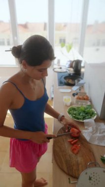 Güzelce aydınlatılmış bir mutfakta, bir kadın taze ve renkli malzemelerin arasında olgun domatesleri ustalıkla dilimler.