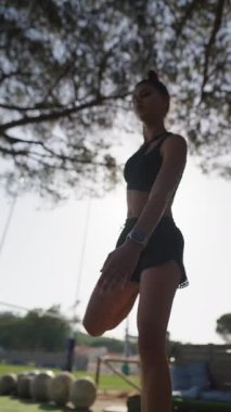 Bir atlet dışarıda esneme egzersizleri yapar, gücünü gösterir ve parlak güneş ışığına odaklanır.