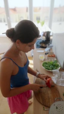 Güzelce güneşli bir mutfakta, bir kadın ustalıkla taze, canlı malzemeleri hazırlar ve doğrar.