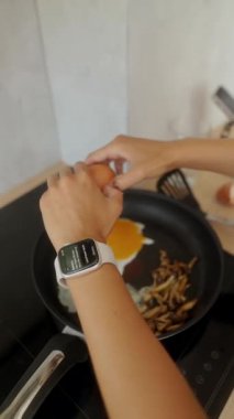 Yetenekli bir birey lezzetli bir yemek yapmak için mantar dolu bir tavaya taze yumurta kırar.