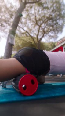 Bir insan açık havada yoga minderinin üzerinde köpük rulo kullanarak dinamik esneme hareketleri yapar.