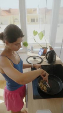 Bir kadın aydınlık bir mutfakta sağlıklı bir yemek hazırlıyor ve ev yemeklerinin ve beslenmenin önemini vurguluyor.