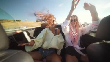 İki kaygısız arkadaş güneşli güneşin altında üstü açık şık bir arabada keyifli bir yolculuğun tadını çıkarıyorlar.