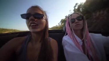 İki yakın arkadaş, parlak, parlak güneşin altında renkli, üstü açık bir arabada neşeyle araba sürüyorlar.